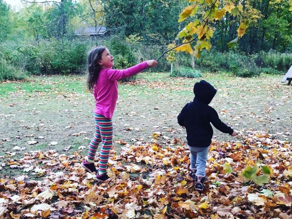 Two children playing in a deep drift of fallen maple leaves on an autumn afternoon