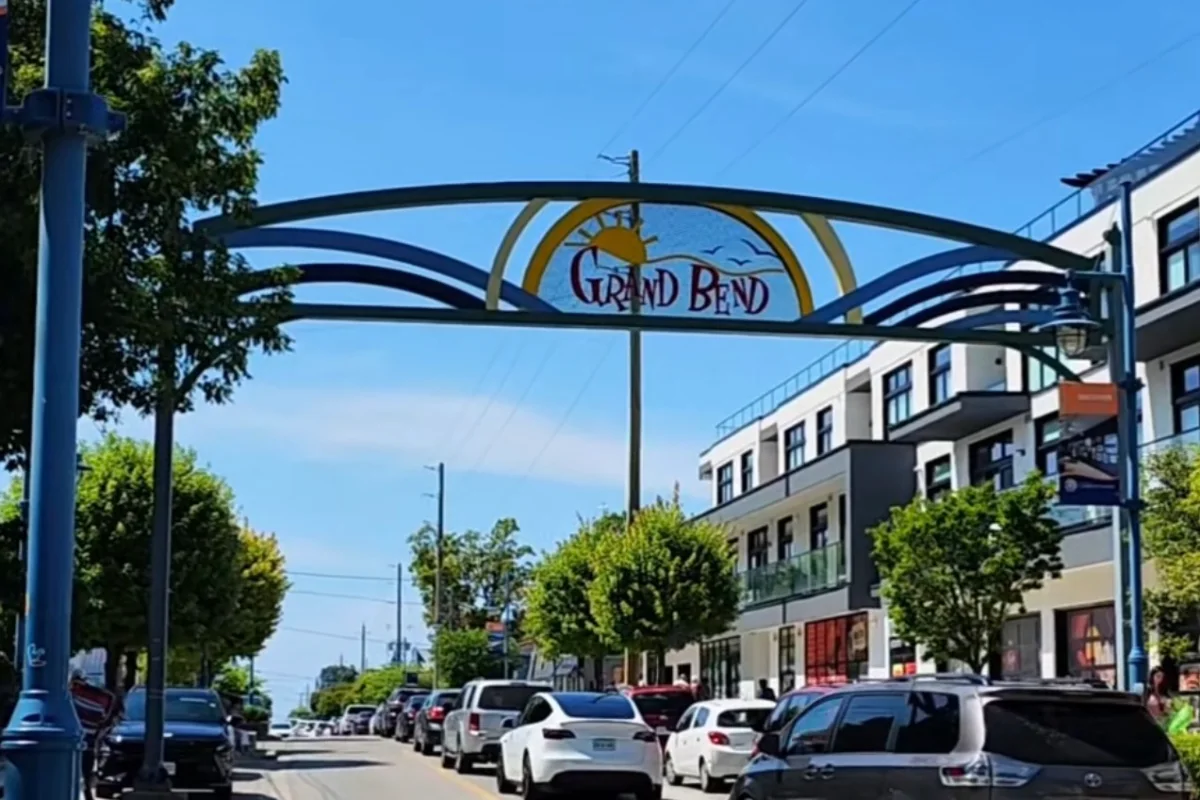 Main Street in Grand Bend on a summer day, under the Grand Bend arch, shops and parked cars on both sides