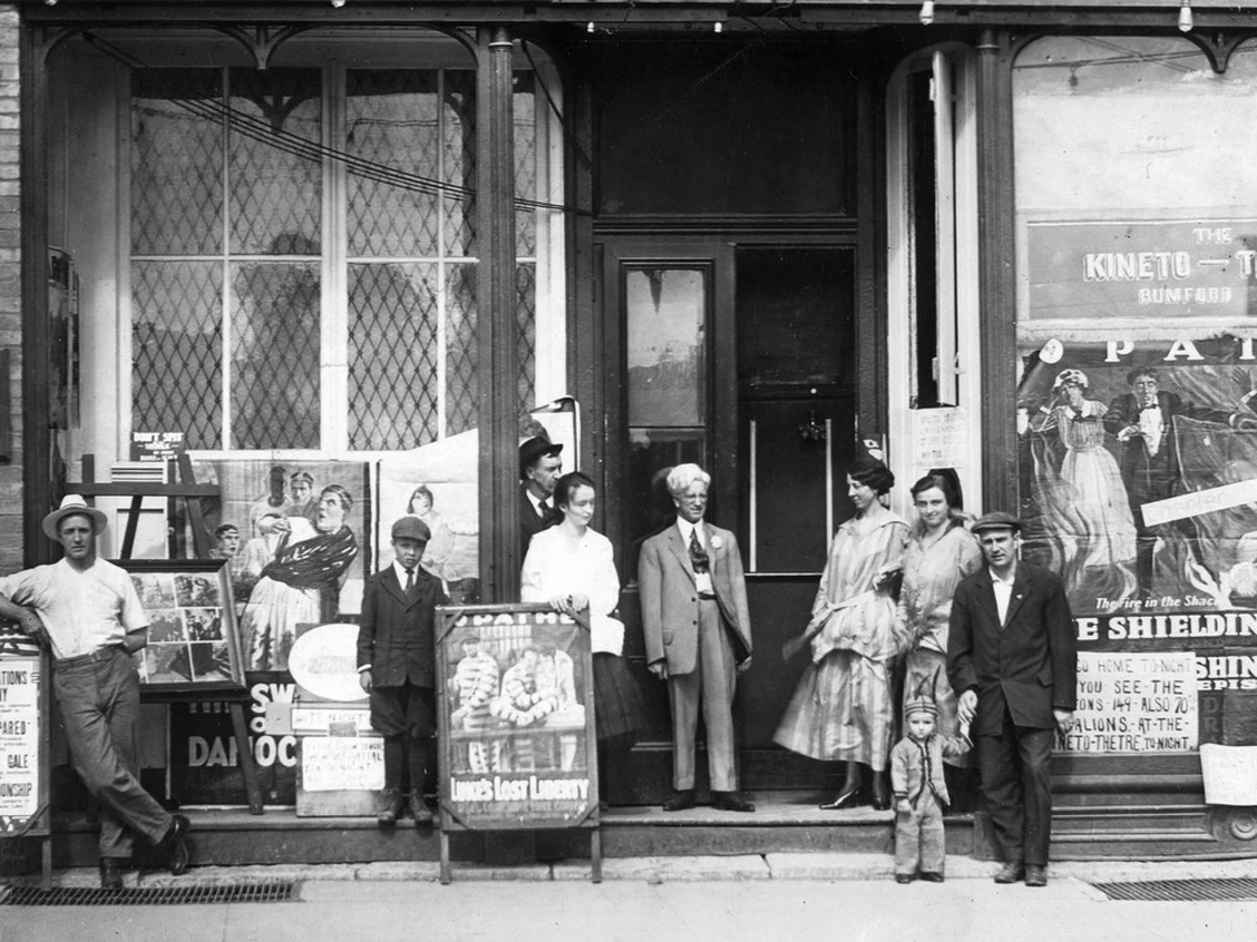 A black-and-white photo of the Kineto Theatre's storefront in Forest, with the Rumford family and staff posing outside among film posters