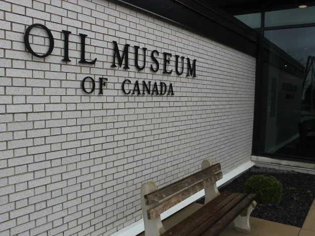 White brick wall of the Oil Museum of Canada with its name in raised black letters beside a bench