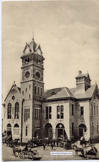 A sepia photograph of Victoria Hall in Petrolia, its clock tower rising above a crowd and horse-drawn carriages on the street