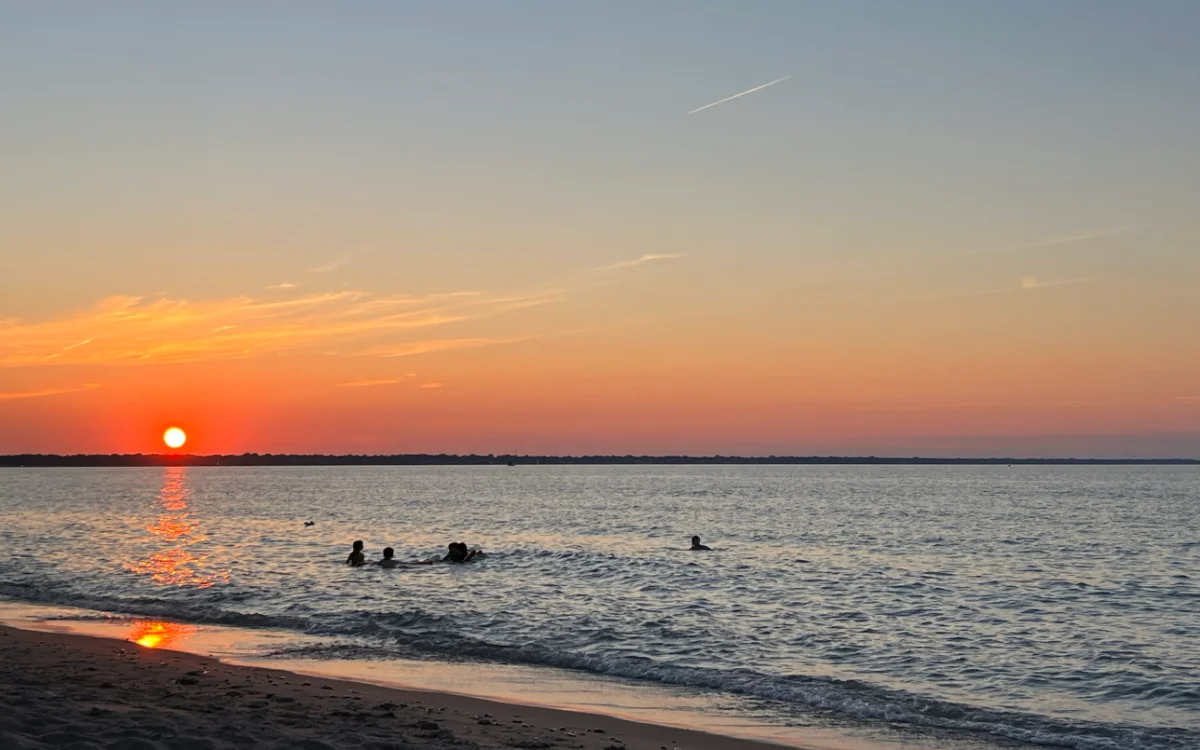 Swimmers in the lake beneath an orange sunset at Bright’s Grove