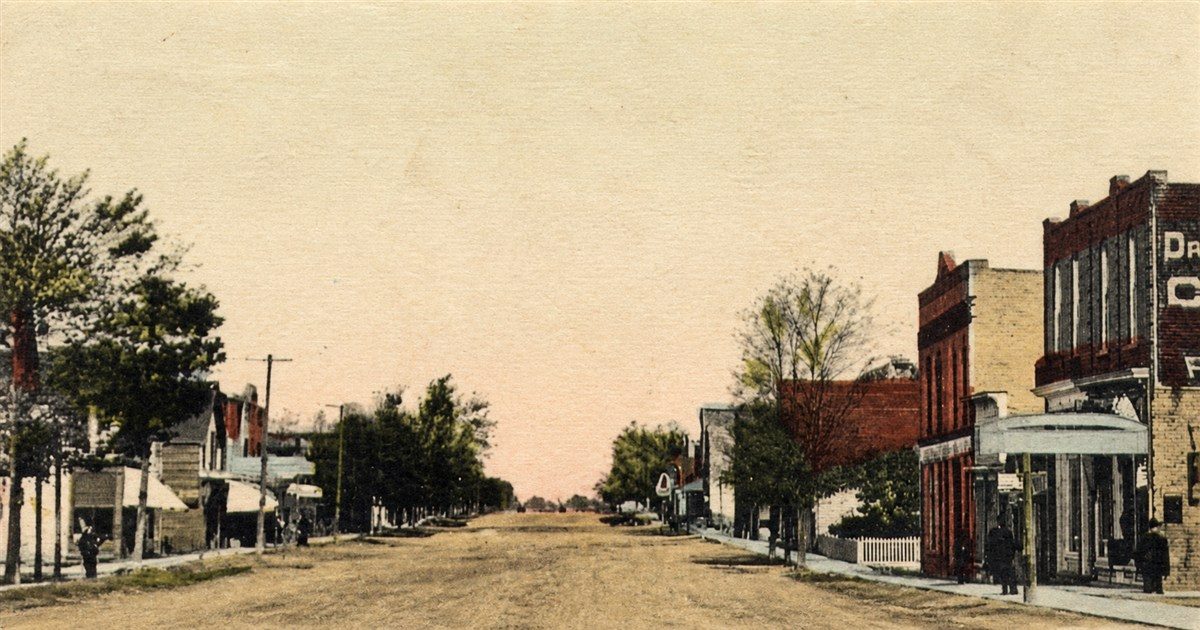 A vintage hand-tinted postcard of Wyoming's main street, a dirt road lined with brick storefronts