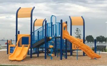 The blue and orange playground structure at Centennial Park in Sarnia, with two slides and the St. Clair River waterfront behind it