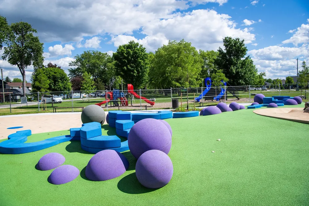 The new splash pad at Kenwick on the Lake Park in Bright's Grove, with purple domes and blue water features on green rubber surfacing, and the playground behind