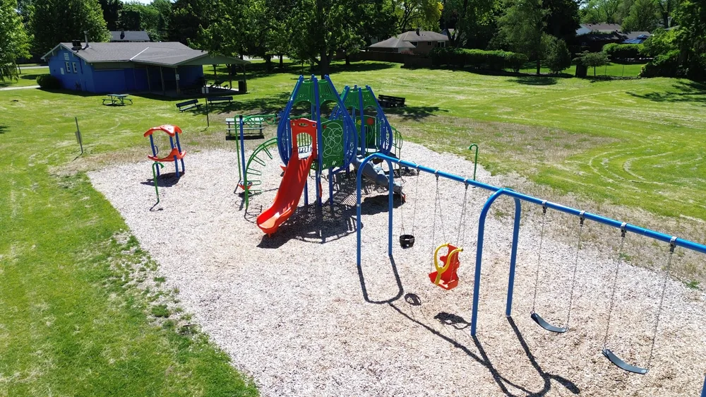 Overhead view of Newton Park playground in Sarnia, showing a blue and green tower with a red slide beside a long swing set with a baby swing