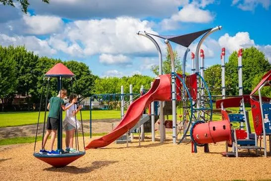 The rebuilt red and grey playground at Sherwood Village Park in Sarnia, with a wide slide, shade sails and a standing spinner