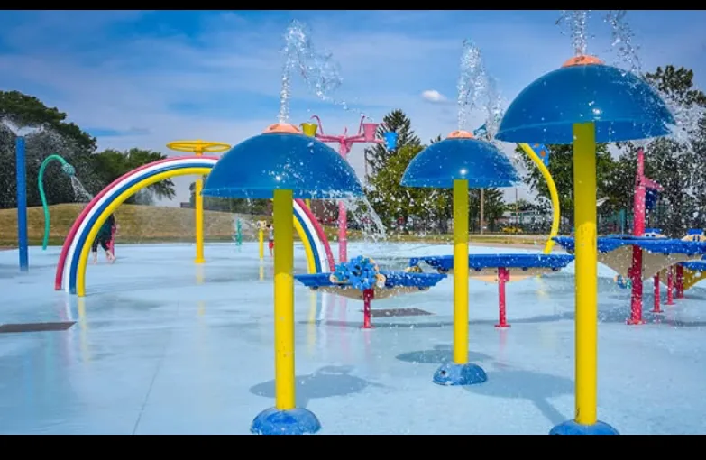 The Tecumseh Park splash pad in Sarnia, with blue mushroom sprayers, a rainbow arch and water jets running across the pad
