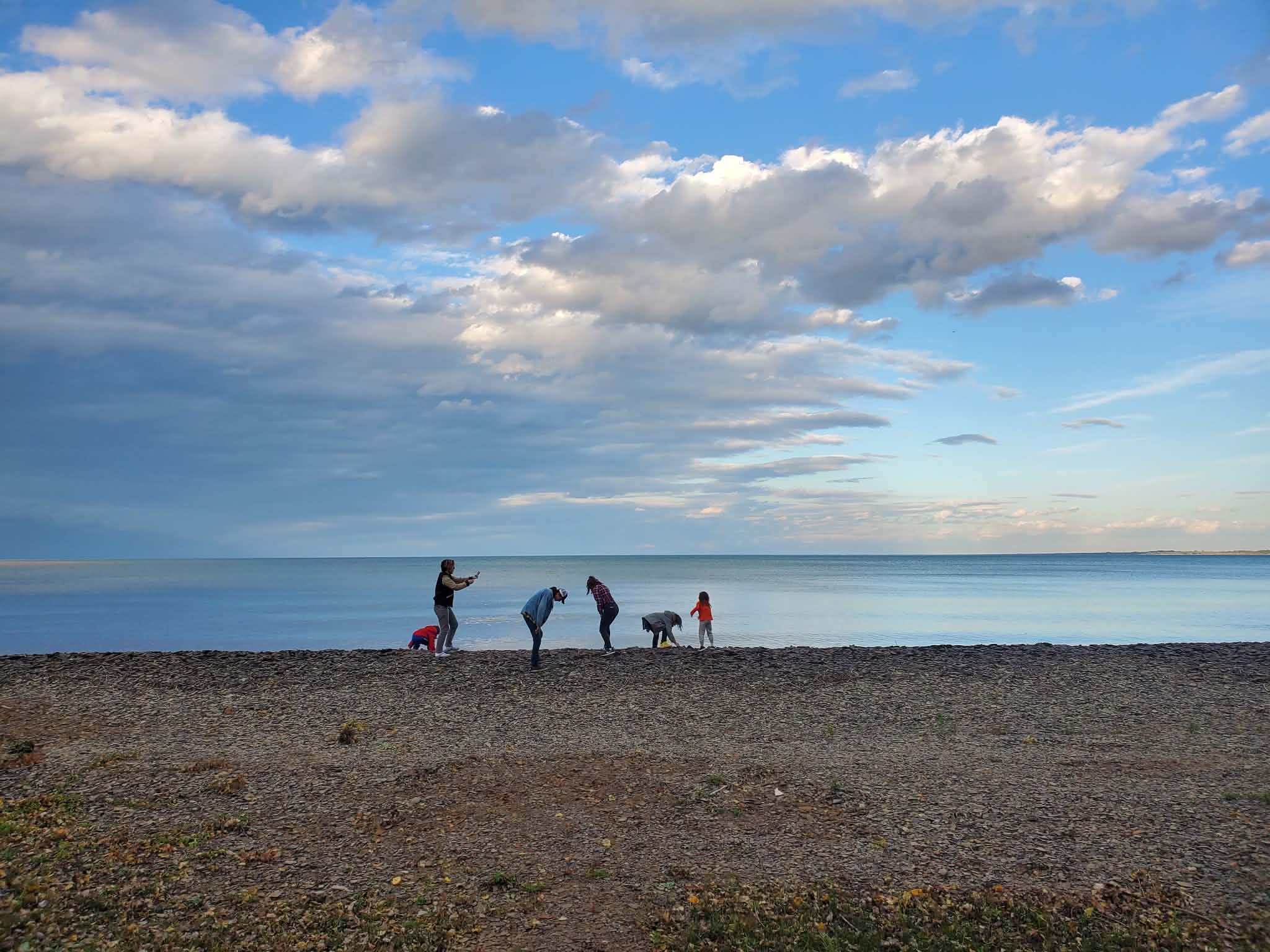 A family exploring the shoreline of Lake Huron under a wide summer sky
