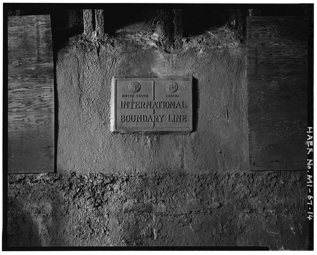 A cast plaque set into the rough concrete wall inside the tunnel, reading United States and Canada above the words International Boundary Line, with a national seal on either side