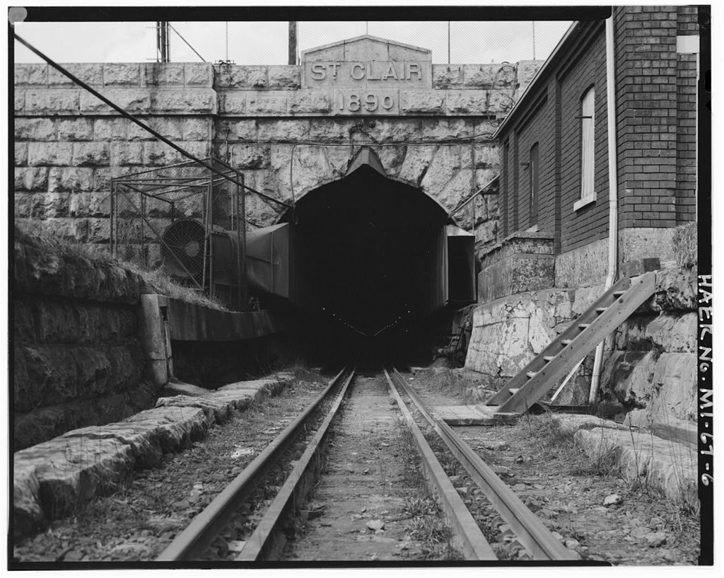 The stone portal of the St. Clair Tunnel head-on, with ST CLAIR 1890 carved into the keystone above the dark bore and rails running in